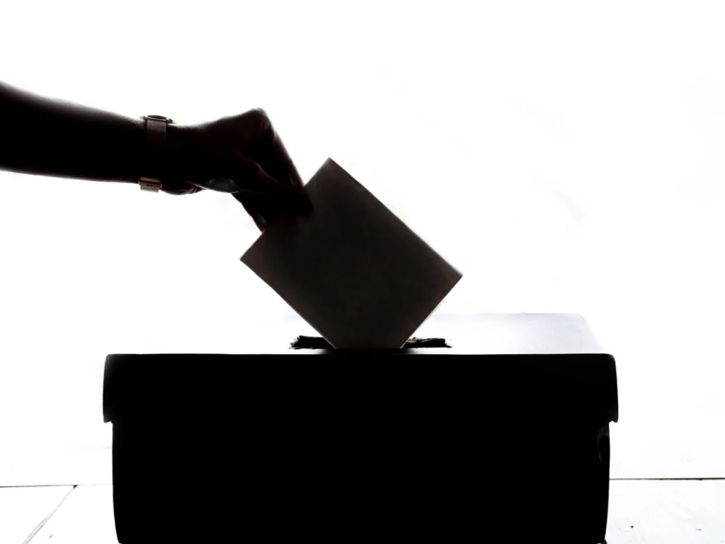 A hand puts a paper in a ballot box